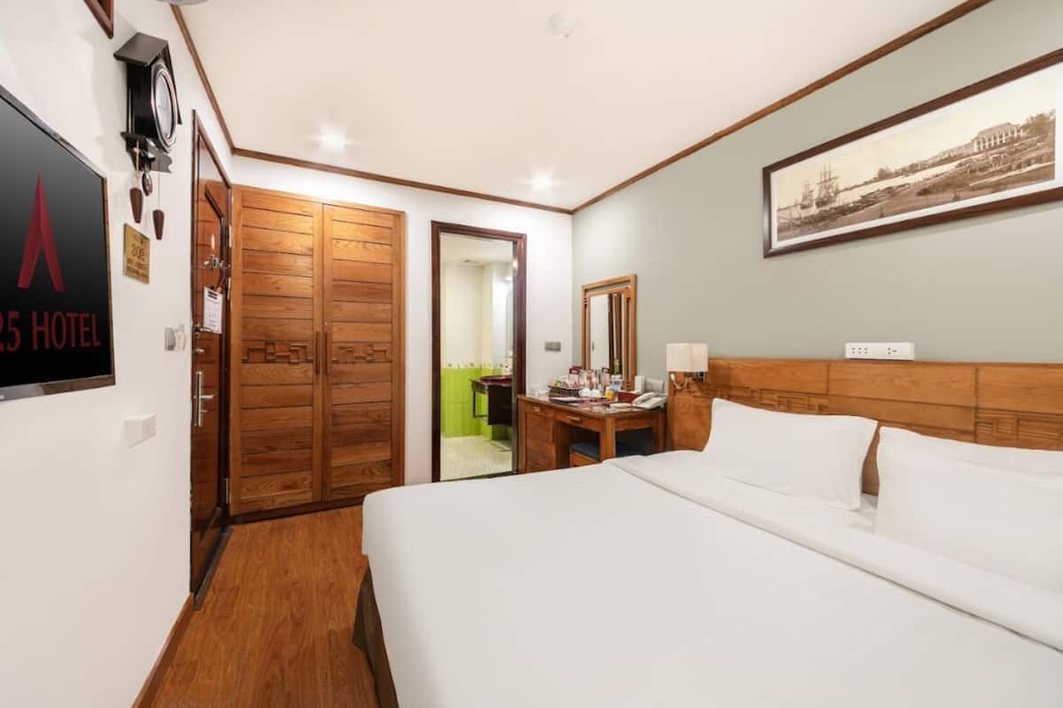 Une chambre d’hôtel avec une armoire en bois, un lit avec du linge de maison blanc, un bureau avec un téléphone et un tableau encadré au mur.