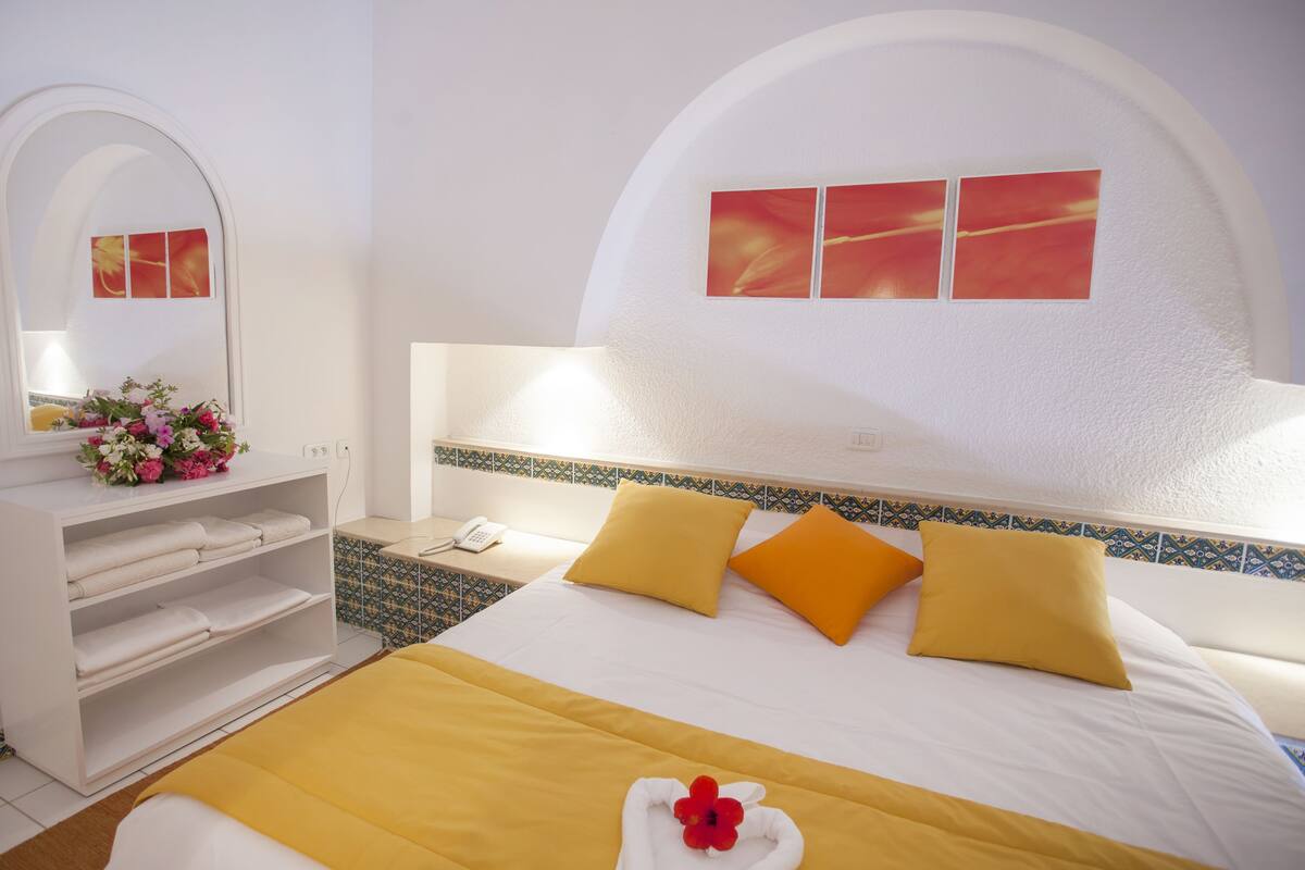A hotel room with a bed, a white console with towels, a mirror, and a wall with a decorative tile border.