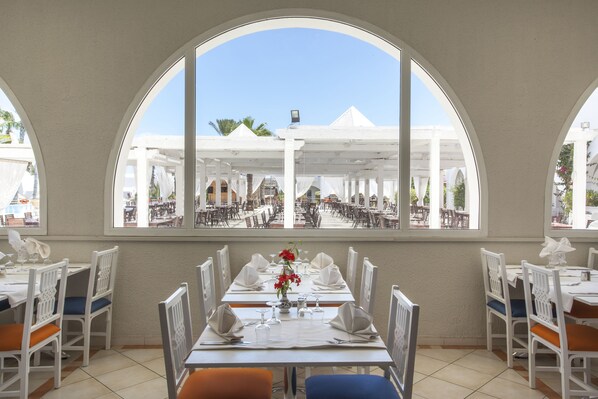 A dining area with white tables and chairs, a large arched window, and a view of outdoor seating.