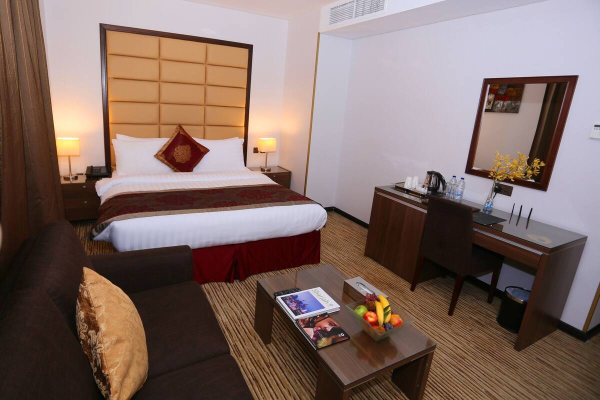 A hotel room with a large bed, a desk, a chair, a coffee maker, and a fruit bowl on the coffee table.