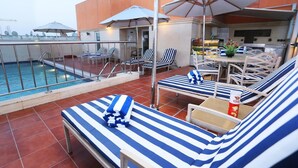 A rooftop pool area with lounge chairs and umbrellas, a pool, and a bar area. - AlHamra Hotel (Sharjah)