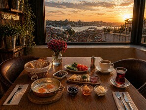 A breakfast table with eggs, bread, cheese, and a view of a cityscape at sunset. - Taksim Prelude Hotel (Istanbul)