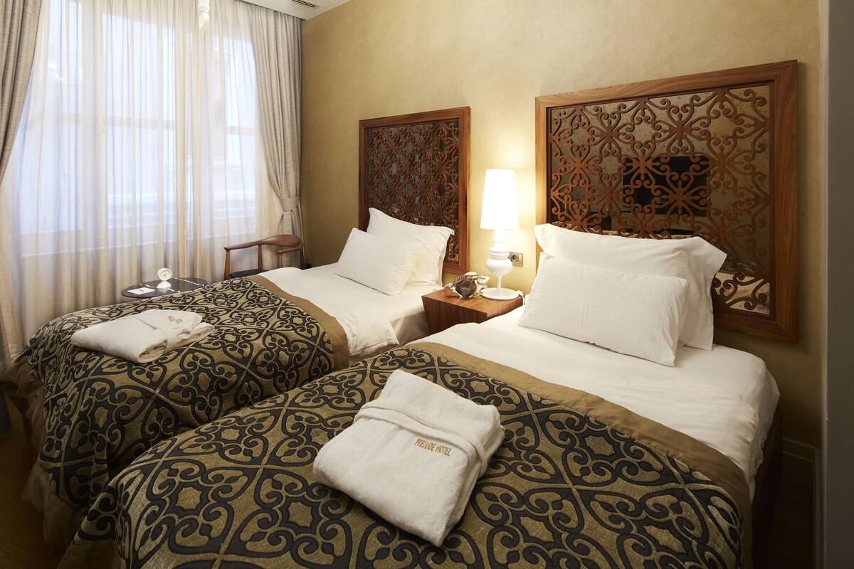 A hotel room with two beds, each with patterned bedding and a white towel on the bed. There is a nightstand with a lamp and a telephone on one side.