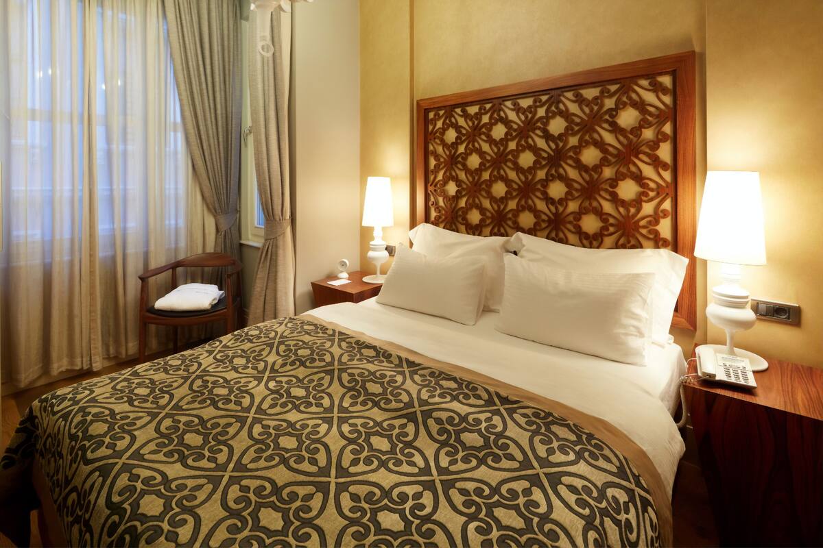 A hotel room with a large bed, two bedside lamps, a wooden headboard, a chair with a towel, and a telephone on the nightstand.