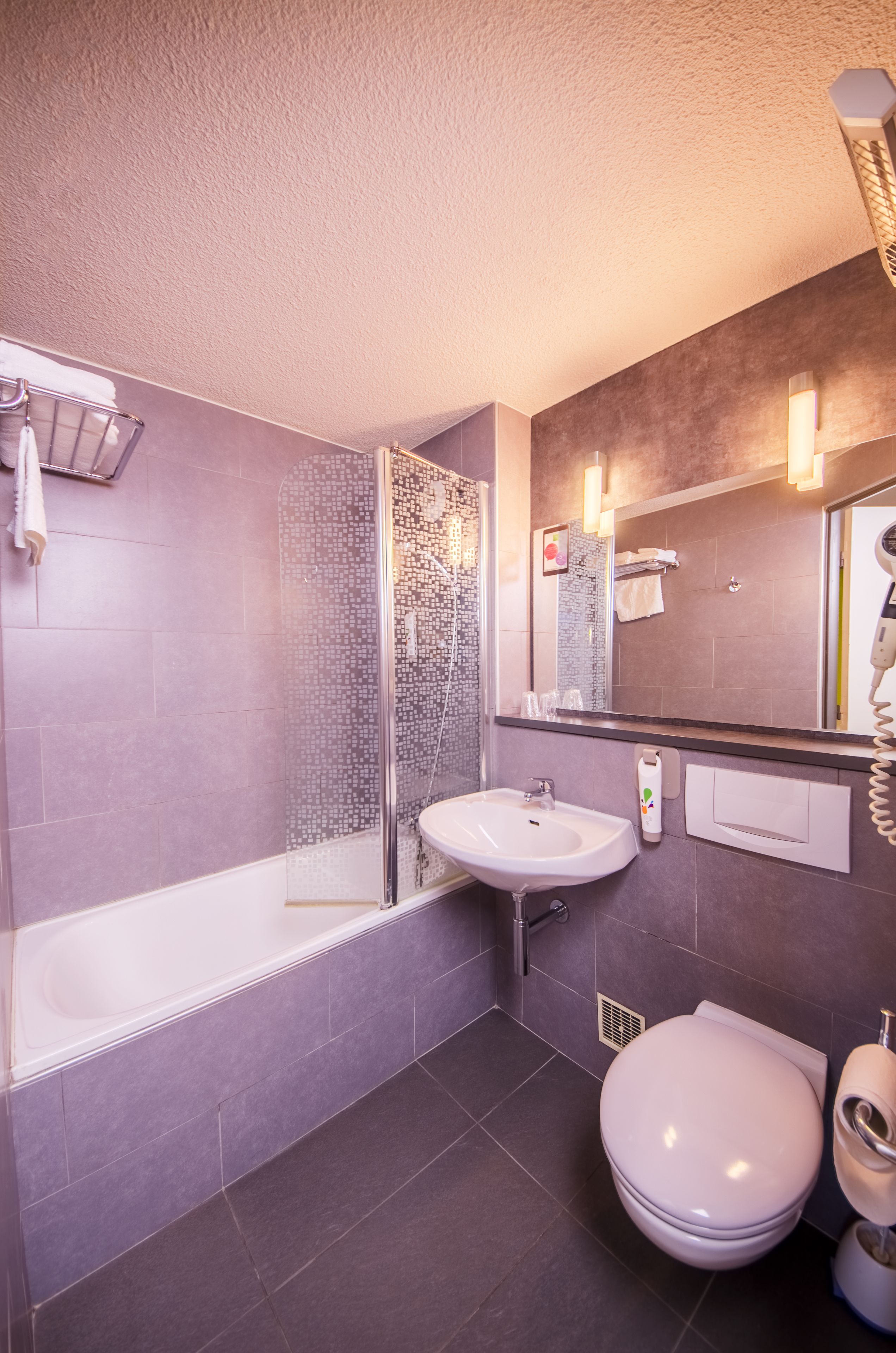 A modern bathroom with a glass-enclosed shower, a white sink, a toilet, and a large mirror.