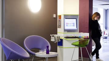 Een receptiegedeelte met paarse stoelen, een kleine tafel met een paarse vaas, en een digitaal scherm op een balie.