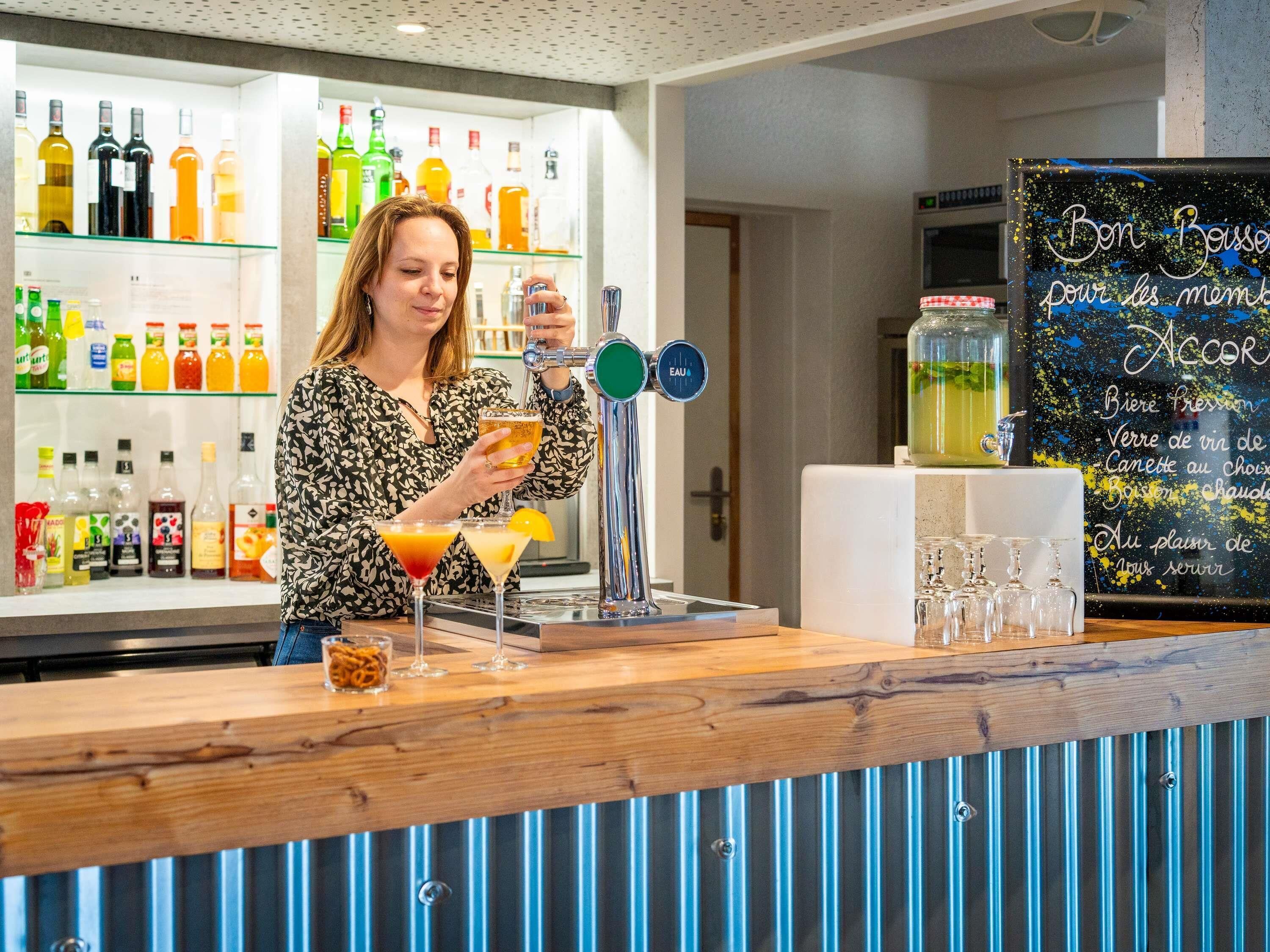Zona de bar con un barman preparando bebidas, una selección de licores embotellados y un menú en una pizarra.
