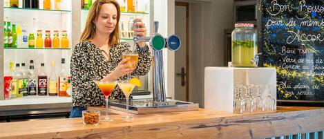 Zona de bar con un barman preparando bebidas, una selección de licores embotellados y un menú en una pizarra.