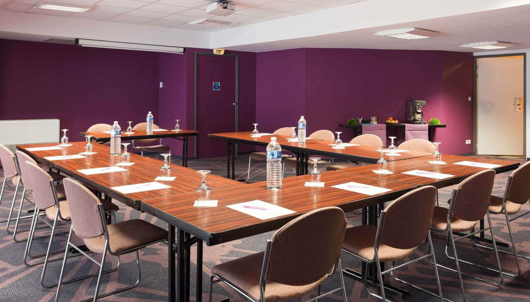 A conference room with long tables, chairs, water bottles, and documents.