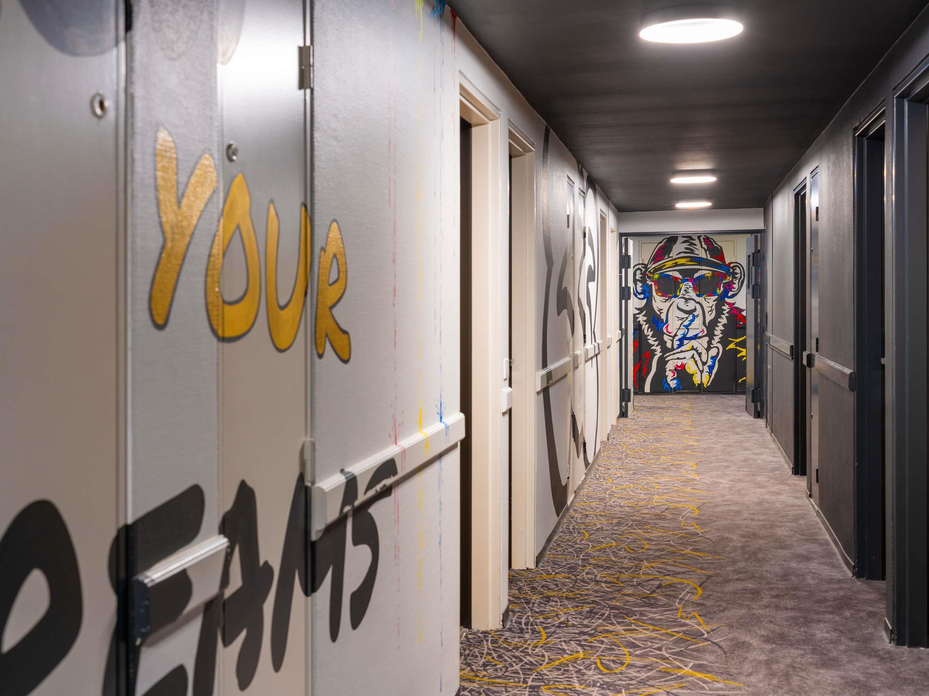 A hallway with a carpeted floor, doors with 'YOUR TEAM' painted on them, and a colorful mural on the wall.