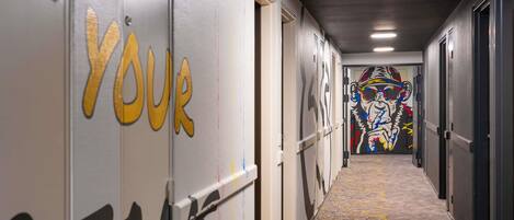 Un pasillo con piso alfombrado, puertas con la leyenda 'YOUR TEAM' pintada y un mural colorido en la pared.