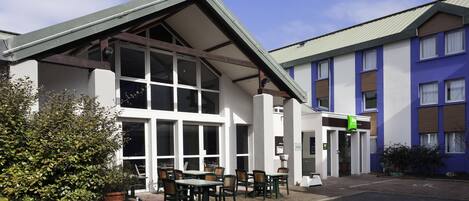 A building with a covered outdoor seating area, large windows, and a sign indicating a business.