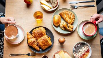 A breakfast table with croissants, cheese, bread, and a bowl of cereal.
