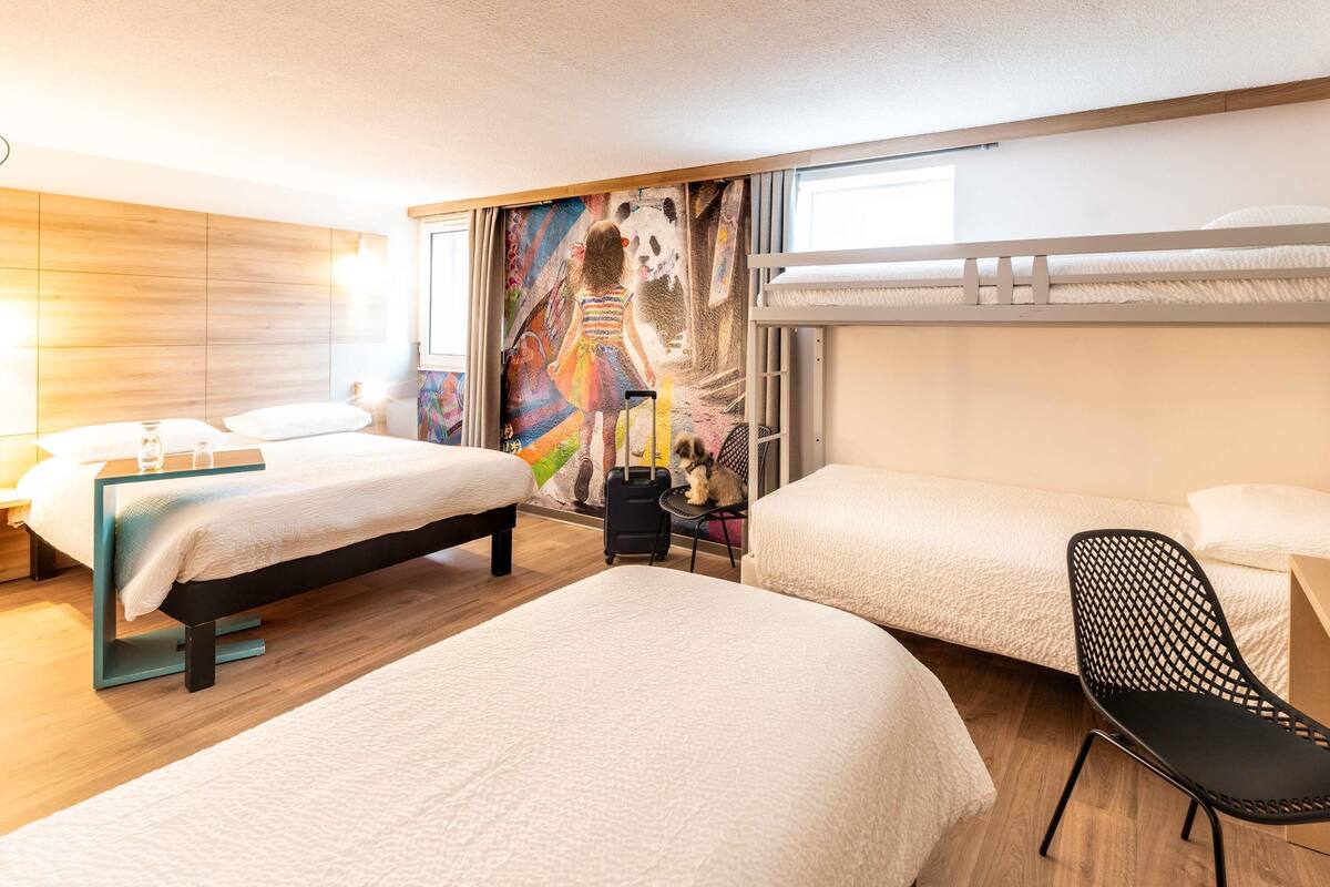 A hotel room with two beds, a mural, a window, and a chair.
