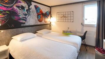 Une chambre d’hôtel avec deux lits, une grande fresque murale, une petite table avec une bouteille et un verre, et une chaise.