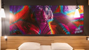 A bedroom with a large wall-mounted TV displaying a colorful tiger image, two bedside lamps, a neatly made bed with white bedding, and a small bedside table with a glass. - ibis Styles Brive La Gaillarde (Brive-la-Gaillarde)
