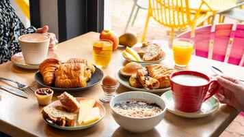A breakfast table with croissants, bread, eggs, and beverages.