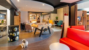 A modern living room with a foosball table, a red sofa, and a dog. - ibis Styles Brive La Gaillarde (Brive-la-Gaillarde)
