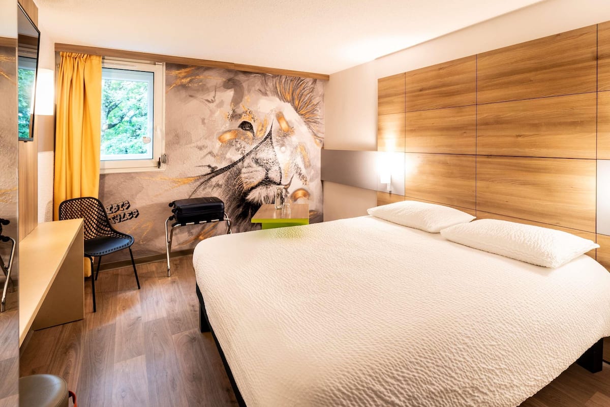 A hotel room with a bed, a desk, a chair, and a mural on the wall.
