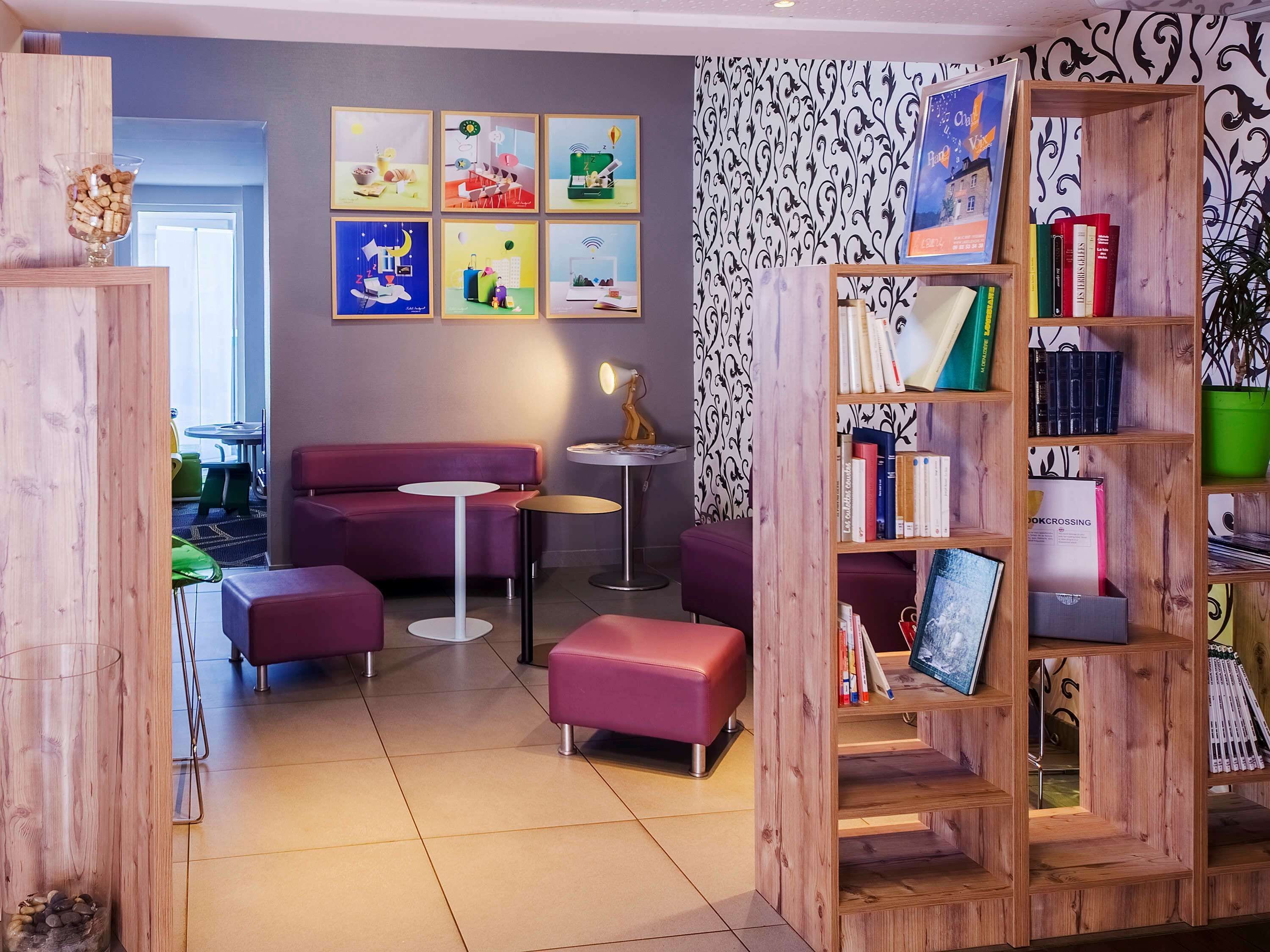 A modern lounge area with a purple sofa, round tables, and a wooden bookshelf filled with books.