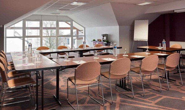 Une salle de conférence équipée d’une longue table, de chaises, d’un écran de projection et de grandes fenêtres.
