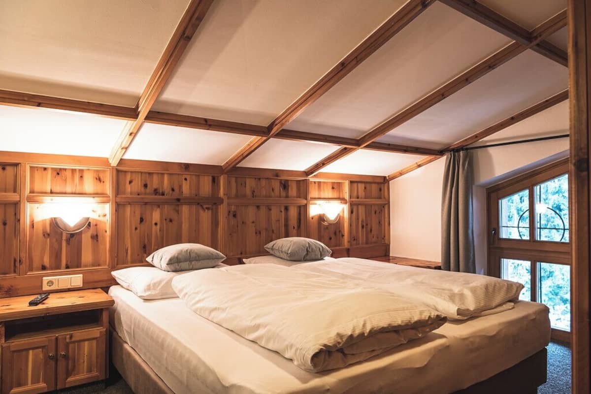 A wooden-paneled bedroom with a bed, bedside lamps, and a window with curtains.