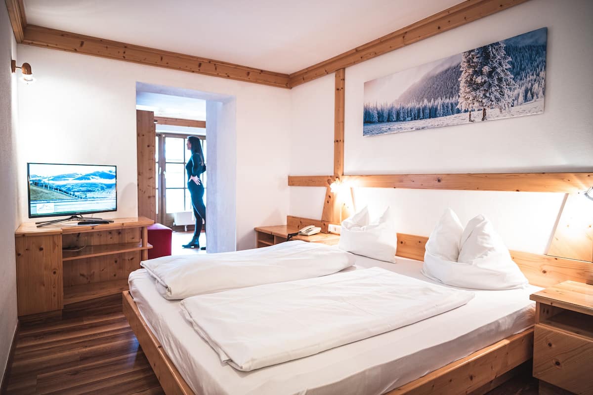 A room with a wooden bed, a desk with a TV, and a painting of a snowy landscape.