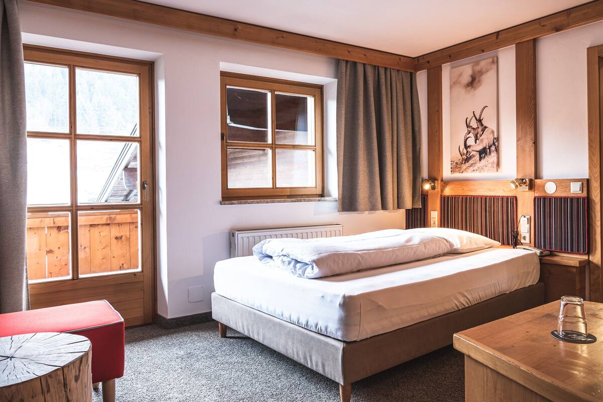A bedroom with a bed, a window, a radiator, a wooden headboard, and a wall-mounted picture.