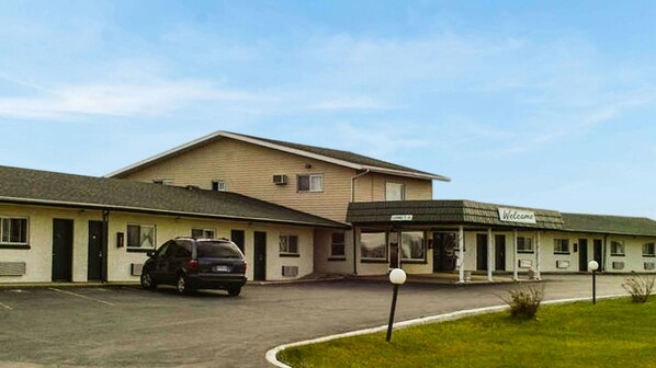 A motel with a parking lot, a covered parking area, and a sign indicating 'Welcome.'