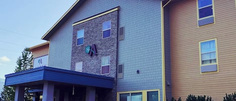 A two-story building with a blue and beige exterior, a large garage door, and a red car parked in front.