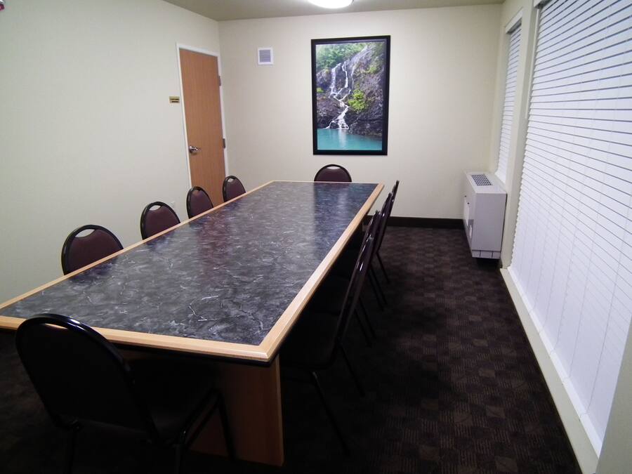 Un salón de conferencias con una larga mesa, sillas, una puerta, un cuadro con una cascada y un equipo de aire acondicionado.