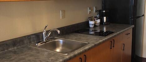 A kitchen with wooden cabinets, a stainless steel sink, a microwave, a coffee maker, and a refrigerator.