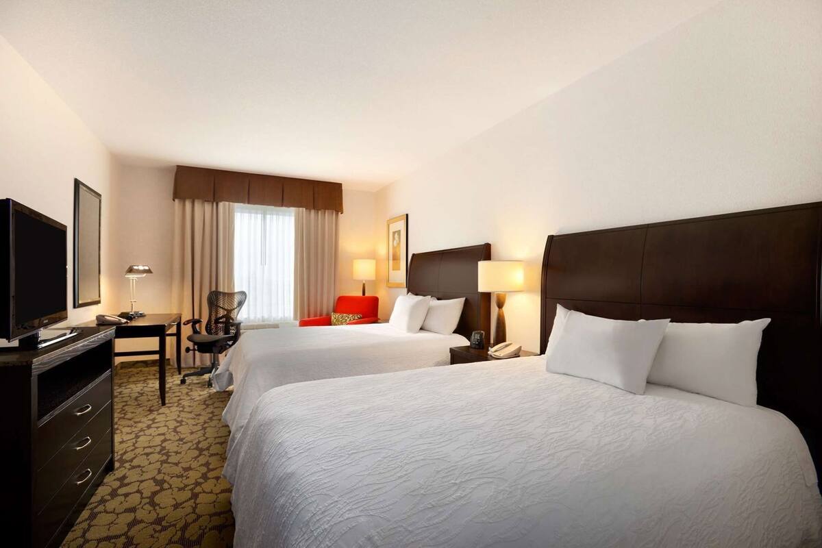 Hotelkamer met twee bedden, een bureau, een stoel, een televisie en een raam met gordijnen.