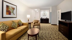 A hotel room with a sofa, armchair, coffee table, TV, and a framed abstract painting.