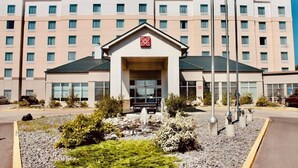 A Hilton Garden Inn hotel with a central entrance, multiple floors, and a landscaped area with a fountain.