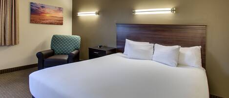 A hotel room with a large bed, a chair, a nightstand, and a painting on the wall.