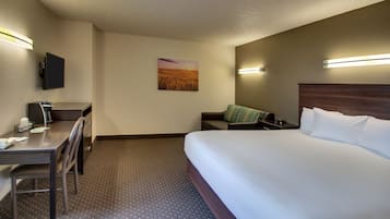 Quarto de hotel com uma cama, uma escrivaninha com cadeira, televisão na parede e um quadro de um pôr do sol.