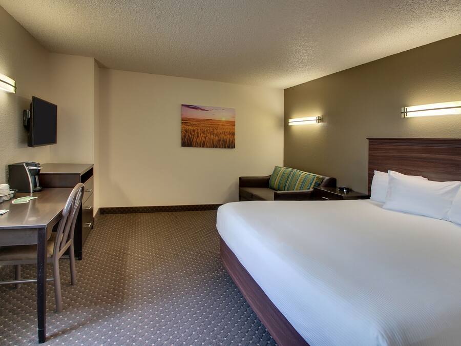 Quarto de hotel com uma cama, uma escrivaninha com cadeira, televisão na parede e um quadro de um pôr do sol.