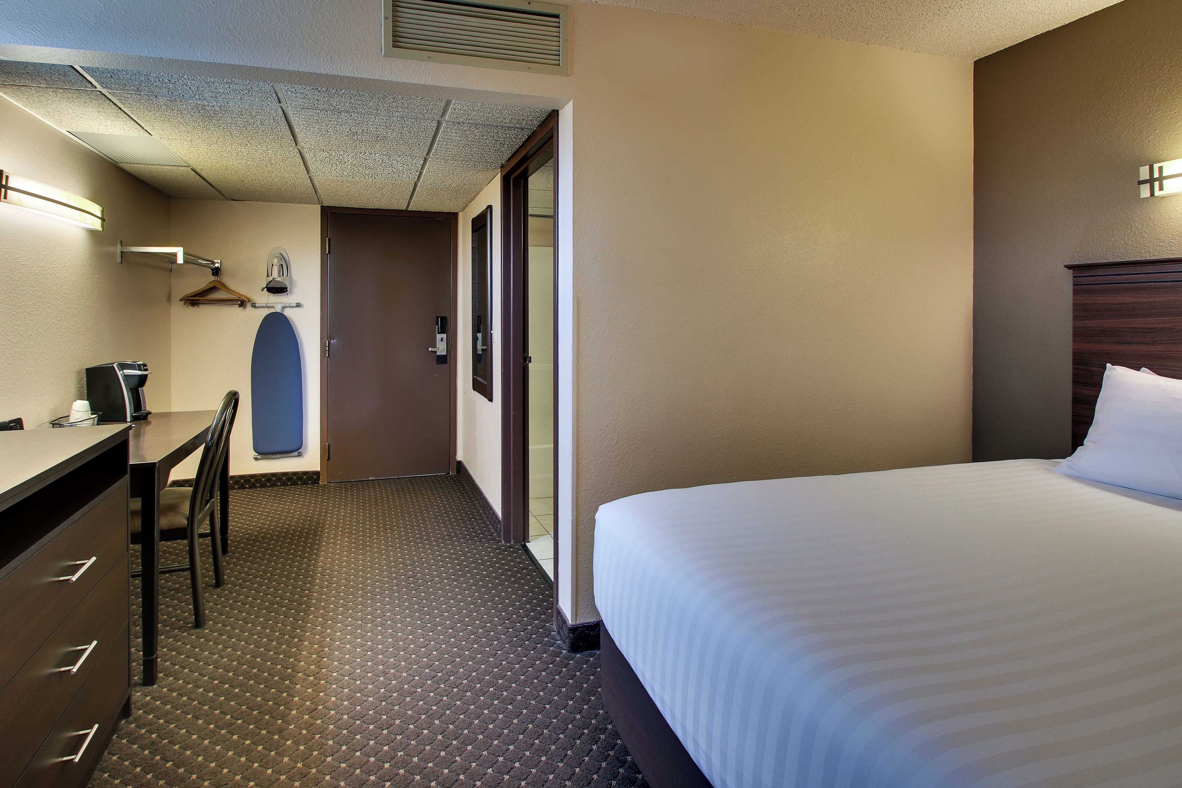 Habitación de hotel con cama, escritorio con silla, perchero y puerta que da a otra habitación.