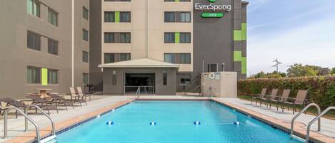 Un hotel con piscina, mobiliario exterior y fachada verde y gris.