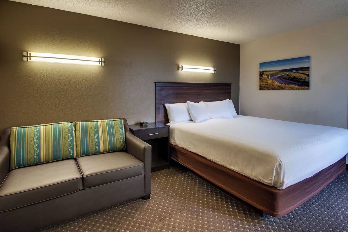 A hotel room with a bed, a sofa, a nightstand, and a wall-mounted picture.