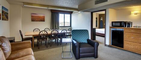 Habitación de hotel con comedor, kitchenette, sofá de cuero marrón, sillón azul y una pequeña mesa.