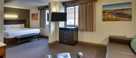 A hotel room with a bed, a desk, a TV, a couch, and a painting on the wall.