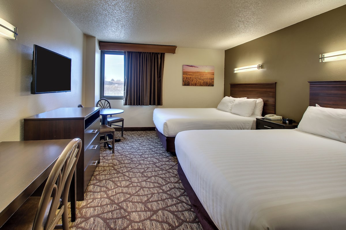 A hotel room with two beds, a desk, a chair, a TV, and a window with curtains.