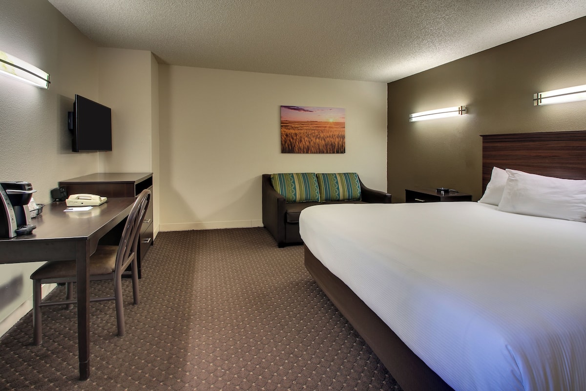 A hotel room with a bed, a desk, a chair, a flat-screen TV, and a painting on the wall.