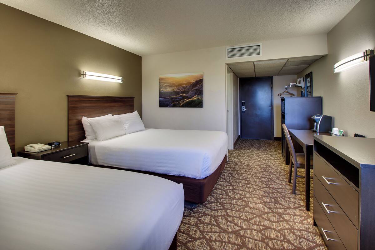 A hotel room with two beds, a desk, a chair, a telephone, and a painting on the wall.