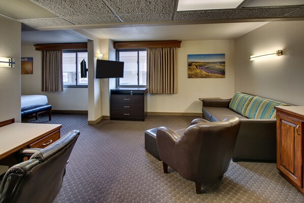 A hotel room with a bed, a desk, a chair, a sofa, a TV, and a window with curtains.