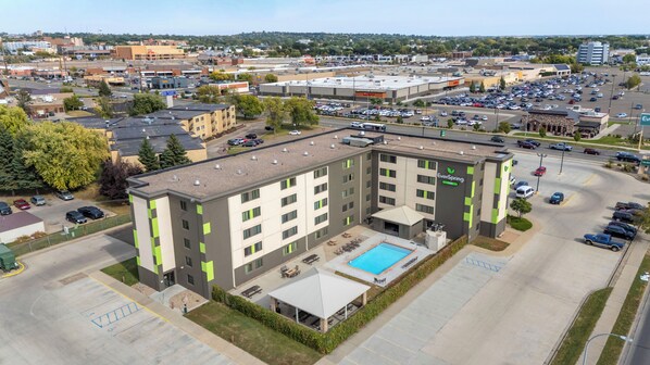 A multi-story hotel with a rooftop pool, parking lot, and a view of the surrounding cityscape.