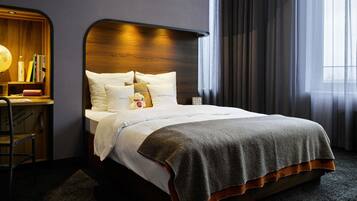 Uma cama bem arrumada com almofadas e um cobertor, uma escrivaninha de madeira com um globo e livros, e uma janela grande com cortinas.