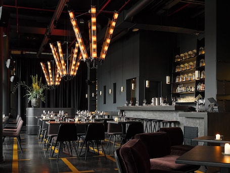 A modern restaurant interior with a bar area, high ceiling, and pendant lighting.. 25hours Hotel HafenCity